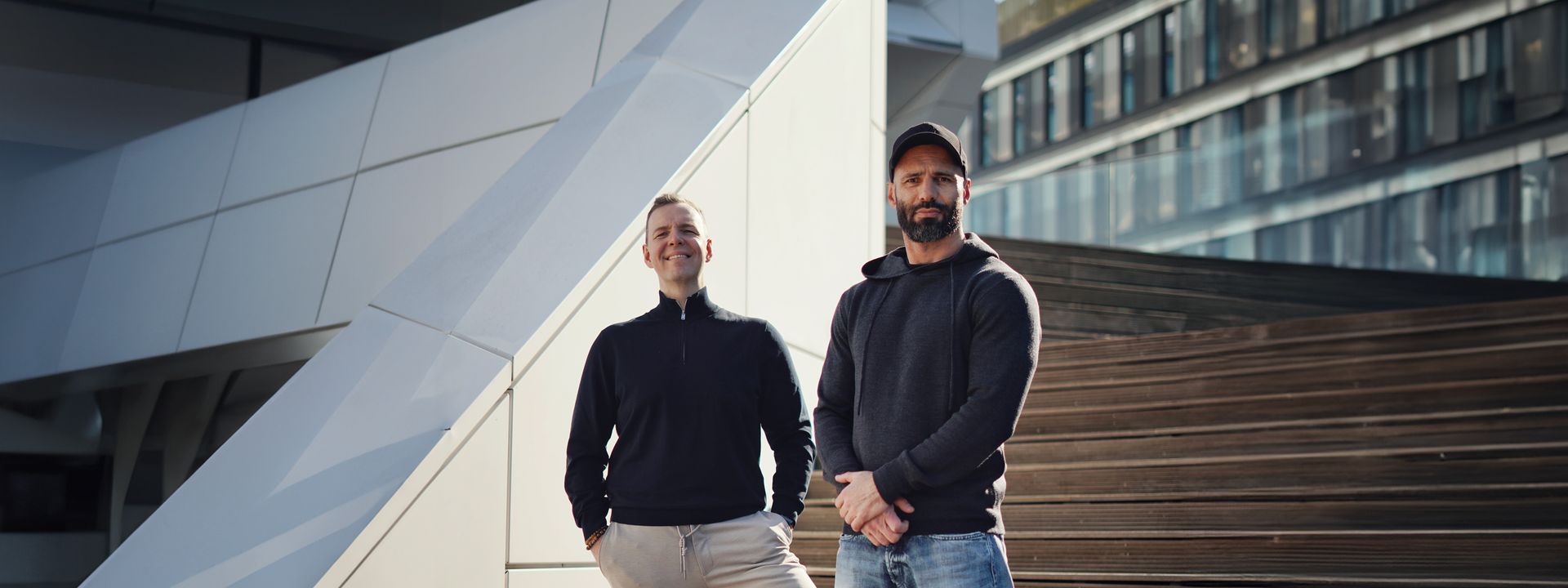 Founder of GreenShift standing confidently on a wide outdoor wooden staircase in a modern urban setting with white geometric architecture in the background.